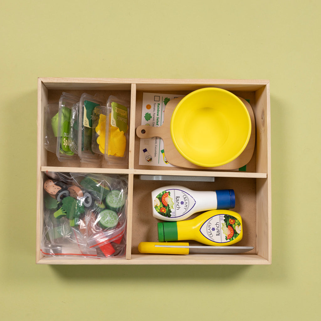 Wooden toy kitchen set with various items including a yellow bowl and bottles on a green background